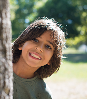 Boy smiling hiding behind the tree