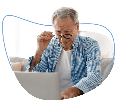 Old man holding his eyeglasses while using laptop