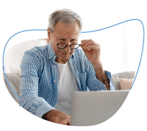 Old man holding his eyeglasses while using laptop